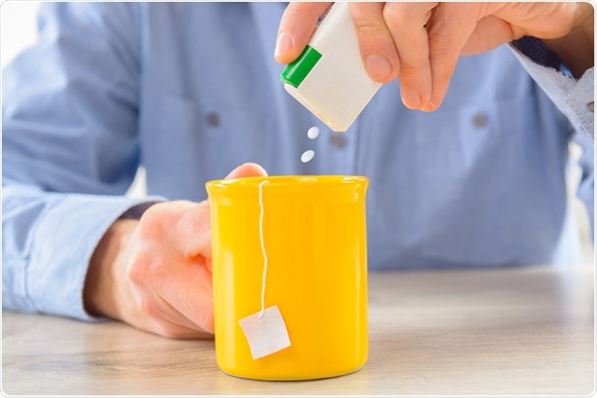 Sweetener tablets and hand with box whit cup of tea. Image Credit: Monika Wisniewska / Shutterstock